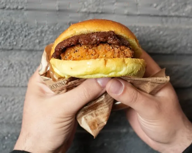 Il Mr Joe tenuto con due mani: la cotoletta di pollo croccante sotto lo smash