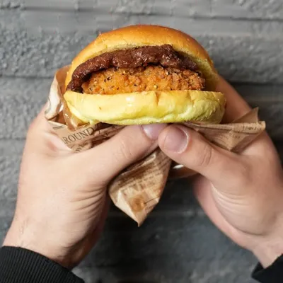 Il Mr Joe tenuto con due mani: la cotoletta di pollo croccante sotto lo smash