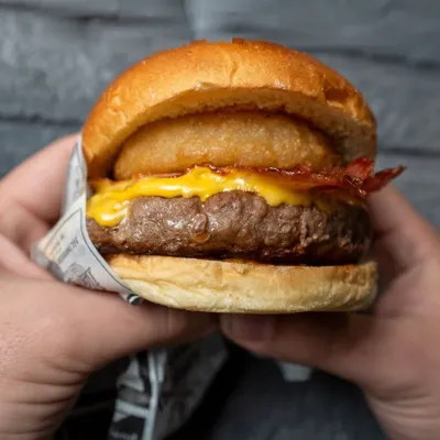 Il Pablo tenuto con due mani: angus alto, cheddar, bacon e l'anello di cipolla